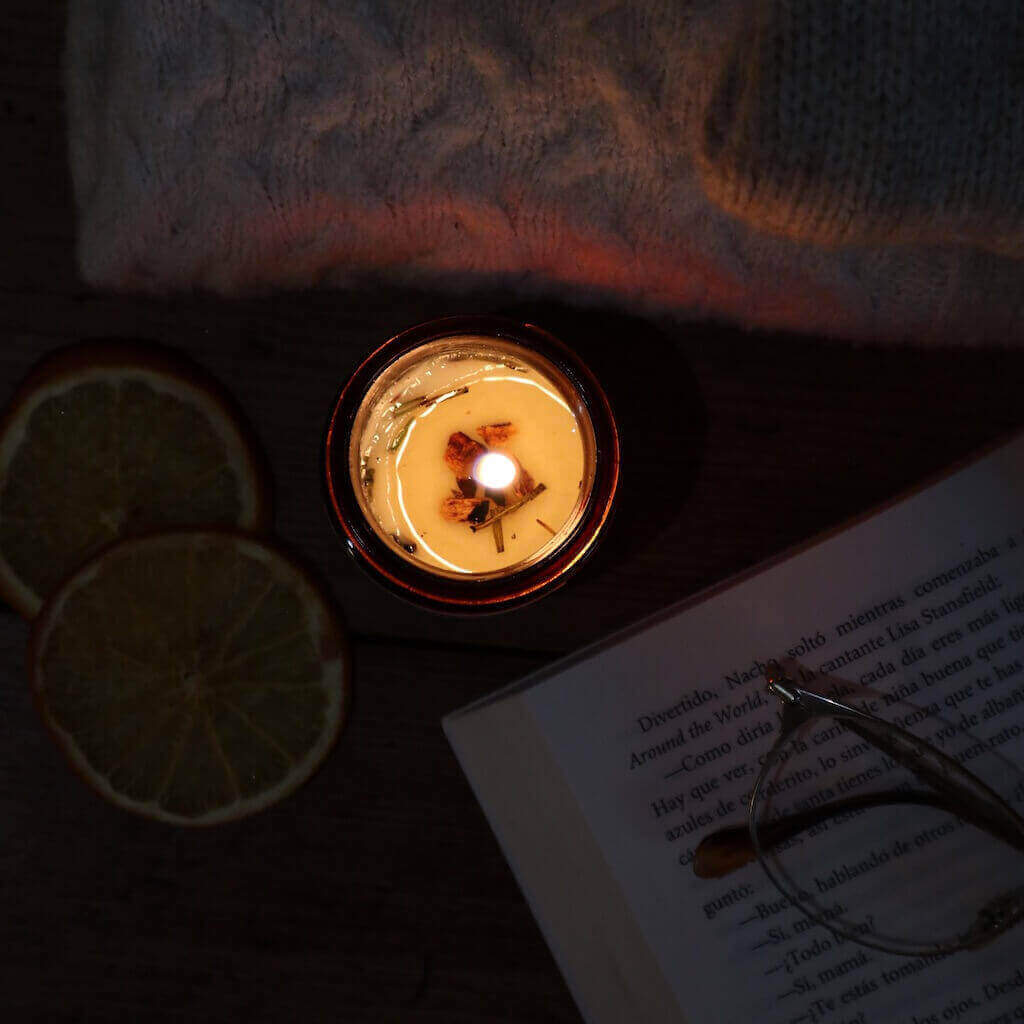 Vela Nº1 ⛰ Romero salvaje de Lullaby Candles encendida en la oscuridad, con libro y rodajas de limón seco